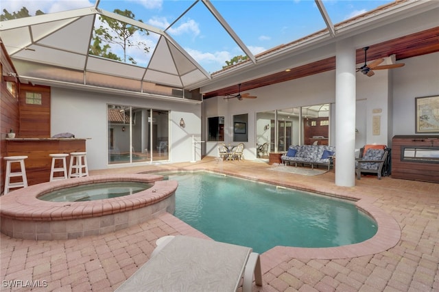 view of swimming pool featuring glass enclosure, ceiling fan, exterior bar, a patio area, and an in ground hot tub