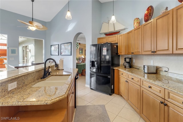 kitchen featuring black fridge, sink, light stone counters, and light tile patterned floors