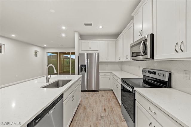 kitchen with light wood-type flooring, light stone counters, stainless steel appliances, sink, and white cabinetry