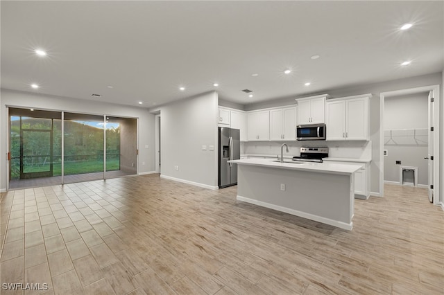 kitchen with appliances with stainless steel finishes, sink, light hardwood / wood-style flooring, white cabinets, and an island with sink