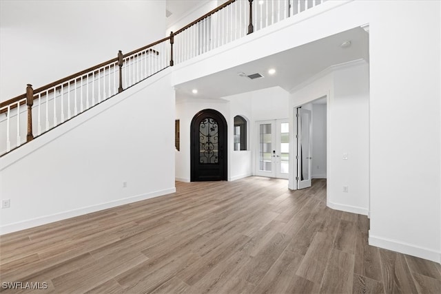 unfurnished living room with hardwood / wood-style floors, french doors, crown molding, and a high ceiling