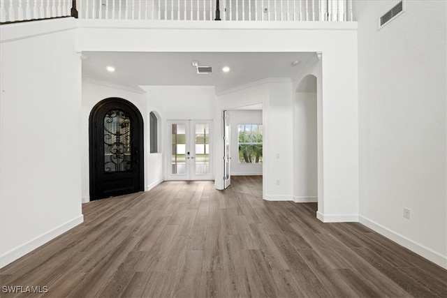 entrance foyer featuring wood-type flooring, crown molding, a high ceiling, and french doors