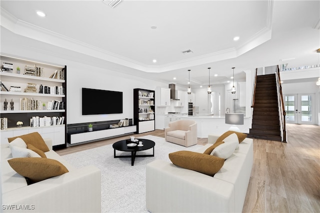 living room with a raised ceiling, crown molding, and light hardwood / wood-style flooring