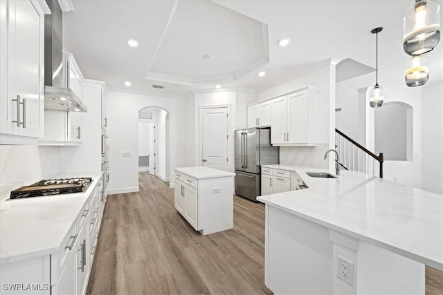 kitchen featuring light wood-type flooring, wall chimney exhaust hood, a kitchen island, decorative light fixtures, and white cabinetry