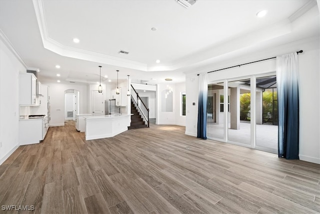 unfurnished living room featuring a raised ceiling, crown molding, and light wood-type flooring