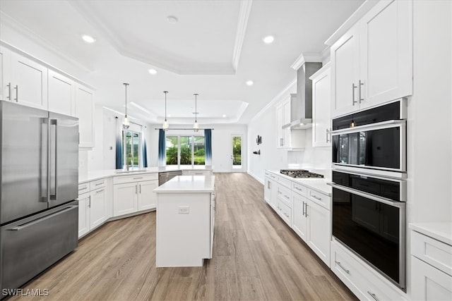 kitchen with stainless steel appliances, kitchen peninsula, decorative light fixtures, a tray ceiling, and light wood-type flooring