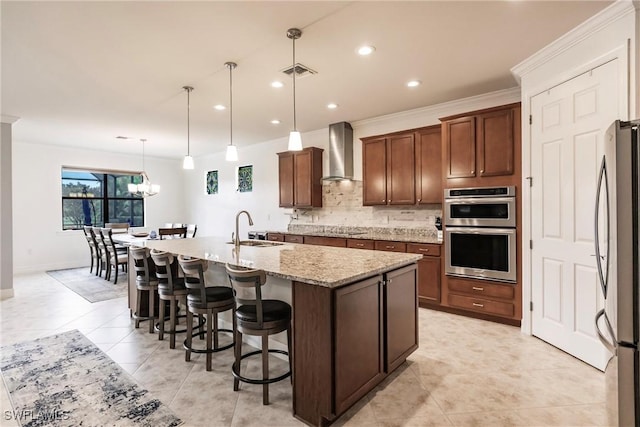 kitchen featuring decorative light fixtures, sink, wall chimney range hood, and an island with sink