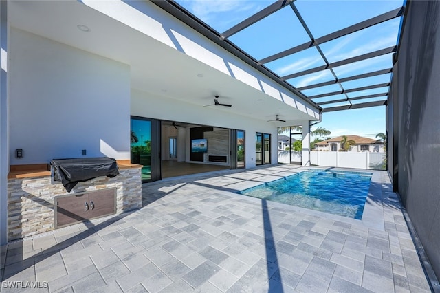 view of swimming pool with glass enclosure, ceiling fan, a patio area, and an outdoor kitchen