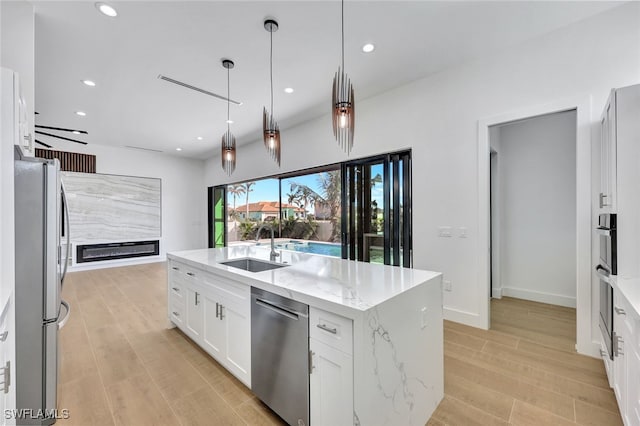 kitchen with white cabinetry, sink, stainless steel appliances, pendant lighting, and a center island with sink