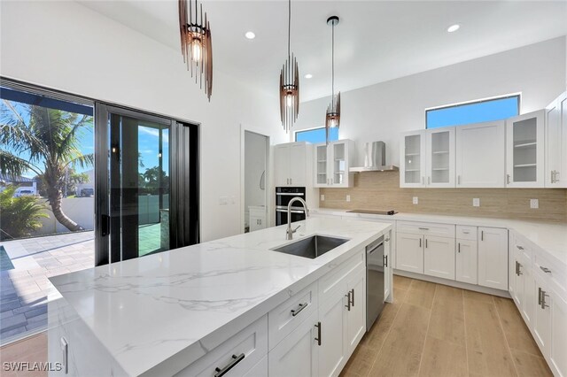 kitchen with sink, wall chimney exhaust hood, stainless steel appliances, a center island with sink, and white cabinets