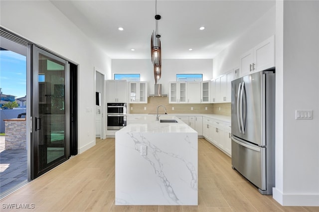 kitchen with white cabinetry, sink, stainless steel appliances, decorative light fixtures, and a kitchen island with sink