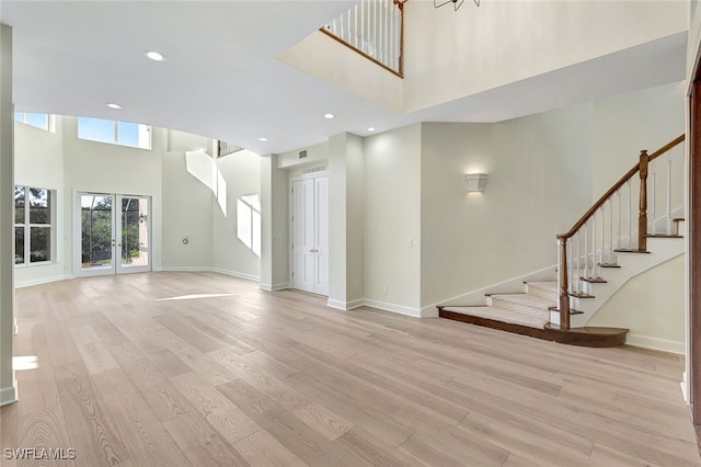 unfurnished living room featuring light hardwood / wood-style flooring, a towering ceiling, and french doors