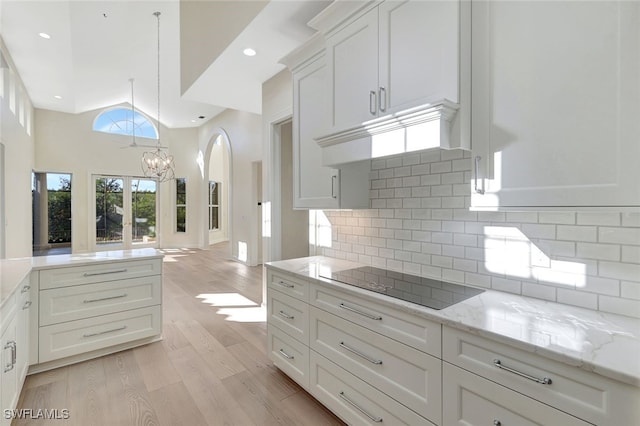 kitchen with light stone counters, light hardwood / wood-style floors, decorative backsplash, black electric stovetop, and white cabinets