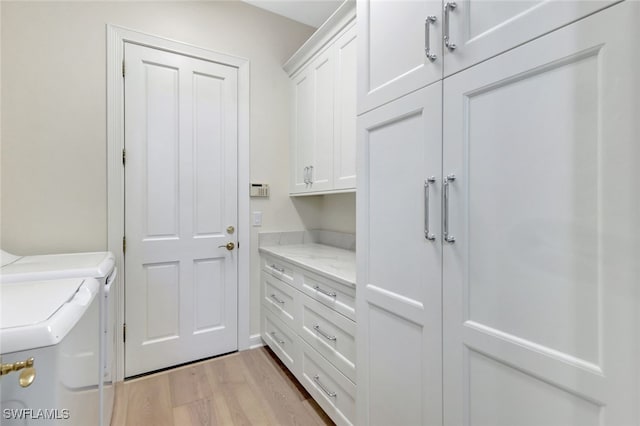 clothes washing area featuring washer and dryer, light hardwood / wood-style flooring, and cabinets