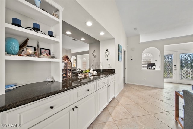 kitchen featuring vaulted ceiling, sink, light tile patterned floors, dark stone countertops, and white cabinets