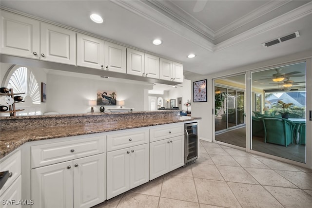 kitchen featuring white cabinets, wine cooler, dark stone countertops, light tile patterned floors, and ornamental molding