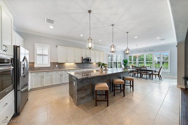 kitchen featuring a kitchen island, appliances with stainless steel finishes, a breakfast bar area, dark stone counters, and hanging light fixtures