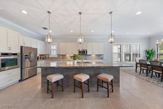 kitchen featuring a breakfast bar, dark stone countertops, appliances with stainless steel finishes, pendant lighting, and a kitchen island with sink