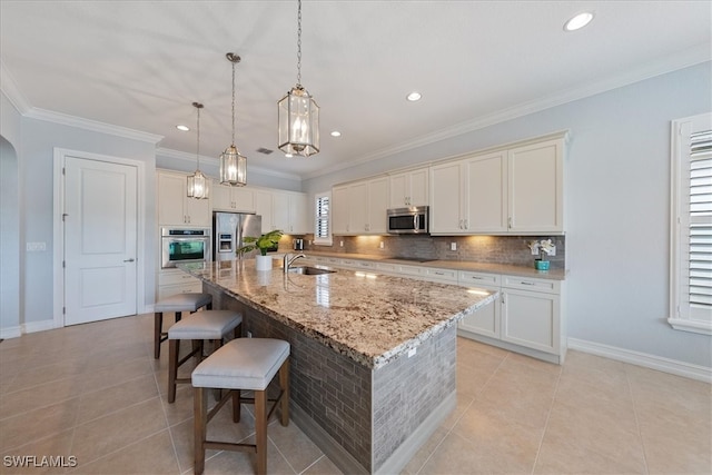 kitchen featuring light stone counters, a large island with sink, appliances with stainless steel finishes, pendant lighting, and decorative backsplash