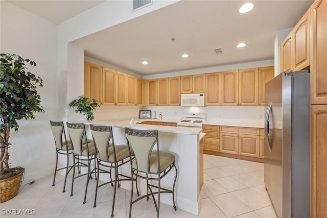 kitchen featuring kitchen peninsula, light brown cabinets, white appliances, and a breakfast bar