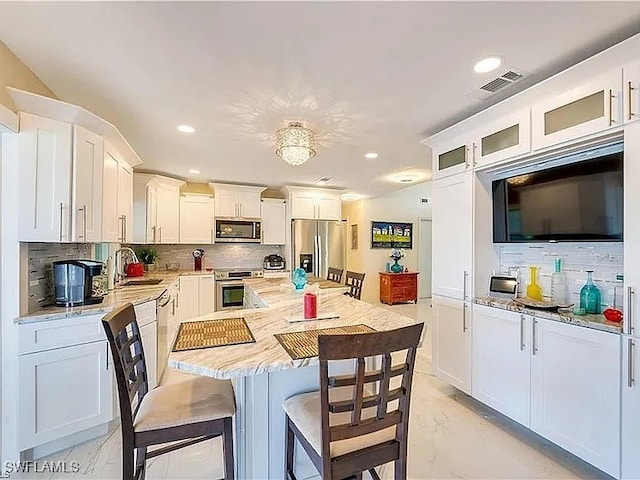 kitchen featuring tasteful backsplash, white cabinetry, light stone countertops, and appliances with stainless steel finishes