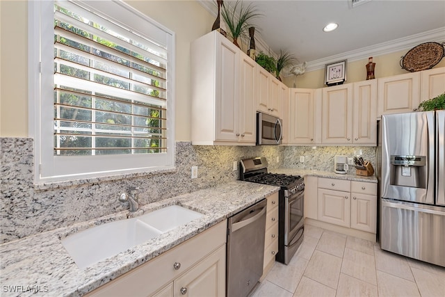 kitchen with sink, ornamental molding, appliances with stainless steel finishes, tasteful backsplash, and light stone counters