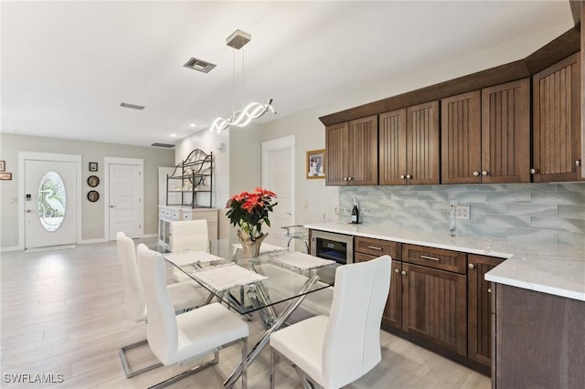 dining space with wine cooler, light hardwood / wood-style flooring, and an inviting chandelier