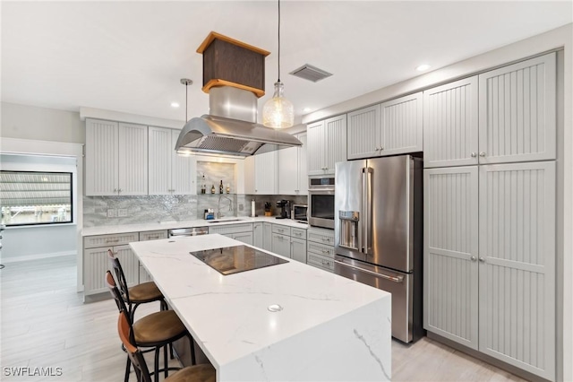 kitchen featuring pendant lighting, sink, stainless steel appliances, a center island, and light stone countertops