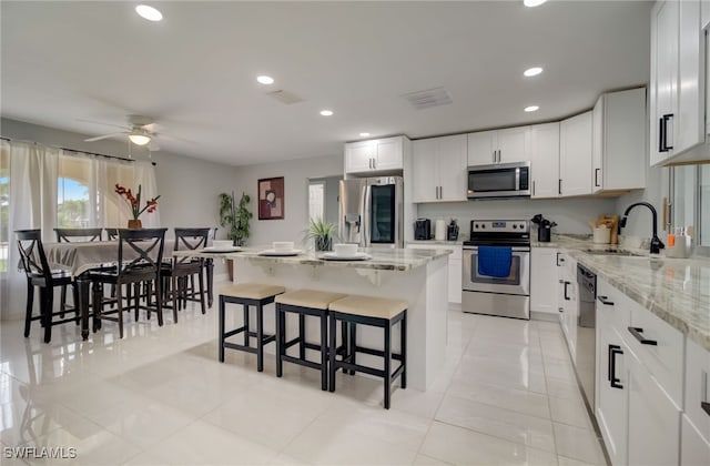 kitchen featuring light stone countertops, stainless steel appliances, sink, white cabinets, and a center island