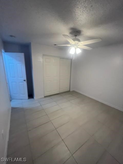 unfurnished bedroom featuring a textured ceiling, a closet, tile patterned floors, and ceiling fan