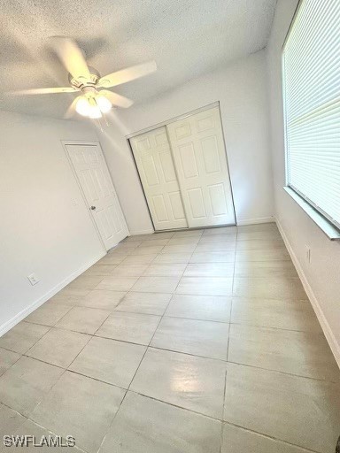 unfurnished bedroom with light tile patterned floors, a textured ceiling, a closet, and ceiling fan