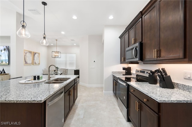 kitchen with a kitchen island with sink, sink, light stone countertops, appliances with stainless steel finishes, and decorative light fixtures