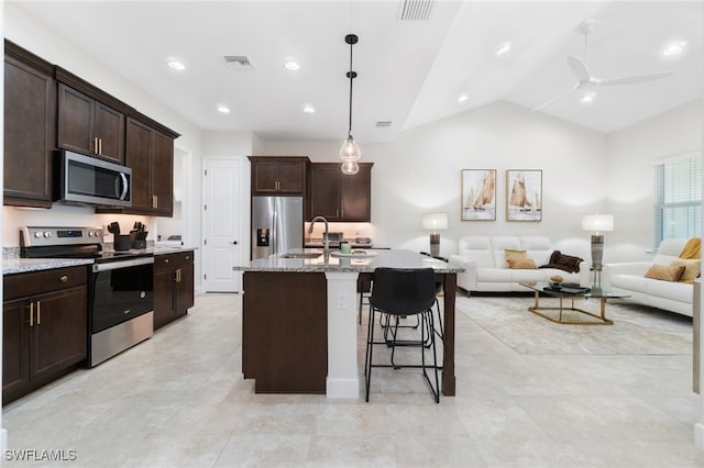 kitchen featuring appliances with stainless steel finishes, dark brown cabinetry, decorative light fixtures, lofted ceiling, and an island with sink