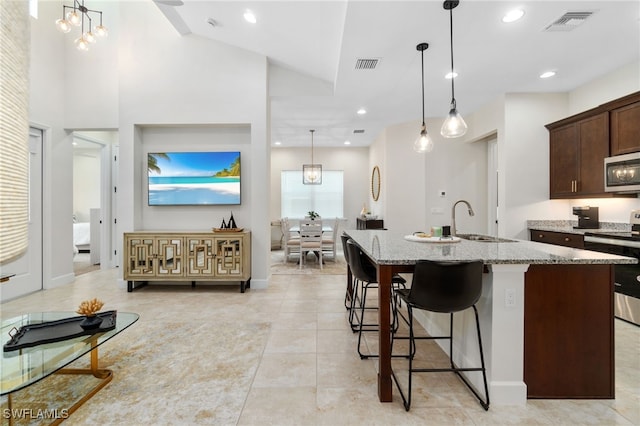 kitchen featuring dark brown cabinetry, sink, hanging light fixtures, stainless steel appliances, and a center island with sink