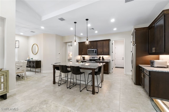 kitchen featuring pendant lighting, light stone counters, a center island with sink, and stainless steel appliances