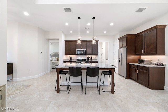 kitchen with hanging light fixtures, light stone countertops, an island with sink, appliances with stainless steel finishes, and dark brown cabinets