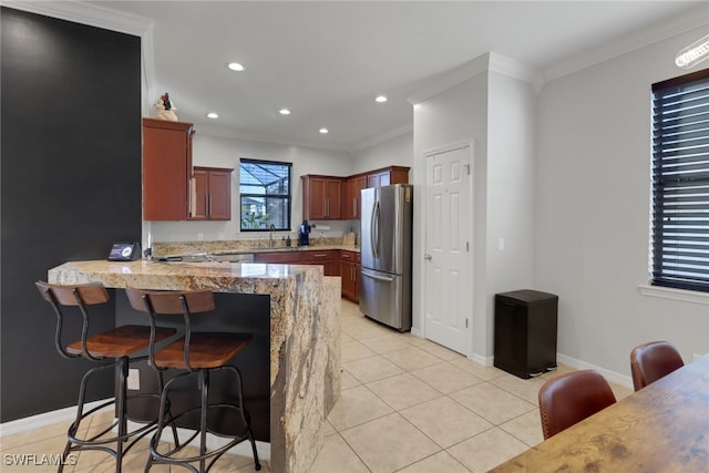 kitchen featuring light stone countertops, light tile patterned floors, ornamental molding, kitchen peninsula, and stainless steel refrigerator