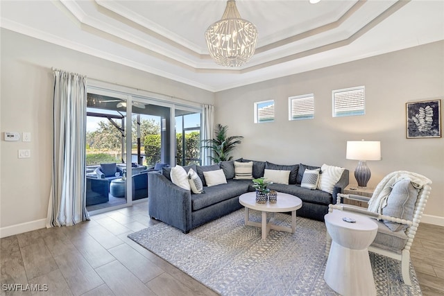 living room with an inviting chandelier, wood-type flooring, ornamental molding, and a tray ceiling