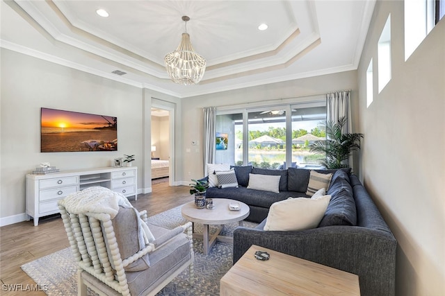 living room with a raised ceiling, wood-type flooring, crown molding, and a chandelier