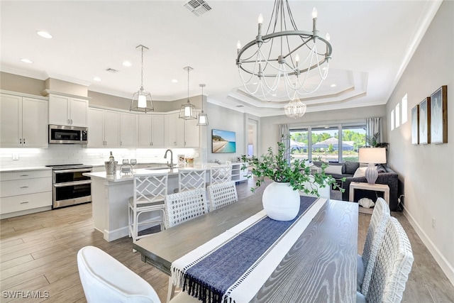 dining space with ornamental molding, a raised ceiling, sink, light hardwood / wood-style flooring, and a notable chandelier