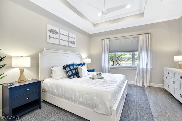 bedroom featuring ceiling fan, a raised ceiling, light wood-type flooring, and ornamental molding