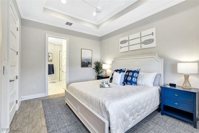 bedroom featuring ensuite bath, a tray ceiling, ceiling fan, crown molding, and light hardwood / wood-style floors