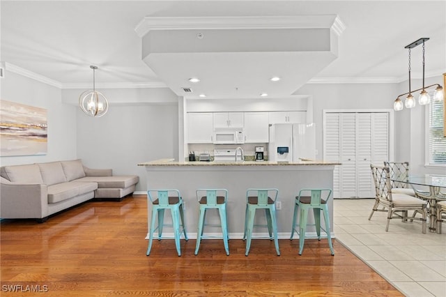 kitchen with white appliances, white cabinetry, a breakfast bar, and ornamental molding