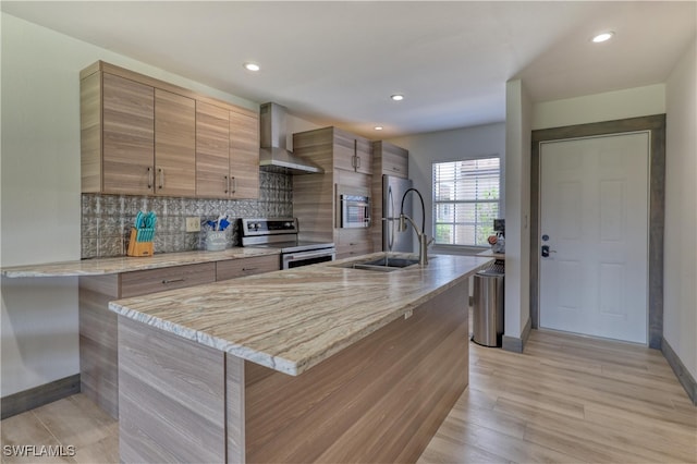 kitchen featuring decorative backsplash, stainless steel appliances, sink, wall chimney range hood, and light hardwood / wood-style flooring