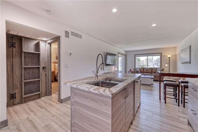 kitchen featuring light stone countertops, sink, stainless steel dishwasher, light hardwood / wood-style floors, and a kitchen island with sink