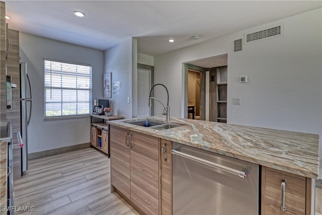 kitchen with light stone countertops, light hardwood / wood-style flooring, stainless steel dishwasher, and sink