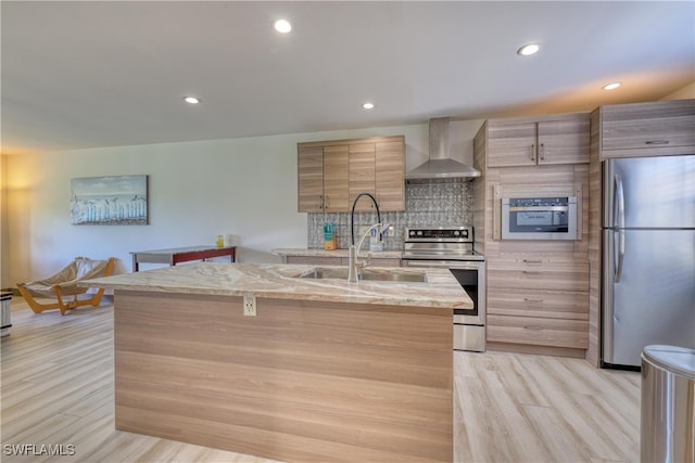 kitchen featuring appliances with stainless steel finishes, light hardwood / wood-style floors, a kitchen island with sink, and wall chimney exhaust hood