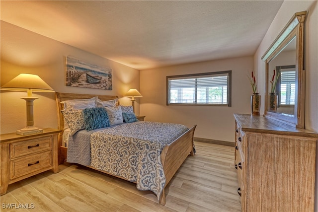 bedroom featuring a textured ceiling, light hardwood / wood-style flooring, and multiple windows