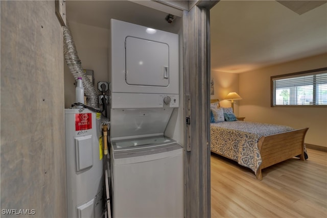 laundry area with electric water heater, stacked washer and clothes dryer, and light wood-type flooring