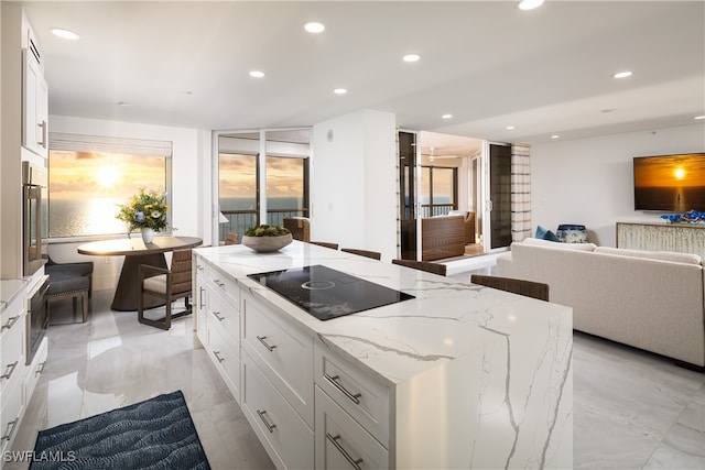 kitchen featuring white cabinets, black electric stovetop, light stone counters, and plenty of natural light